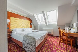 Quarto de hotel com cama, escrivaninha e cadeira. Janela com vista para o exterior.