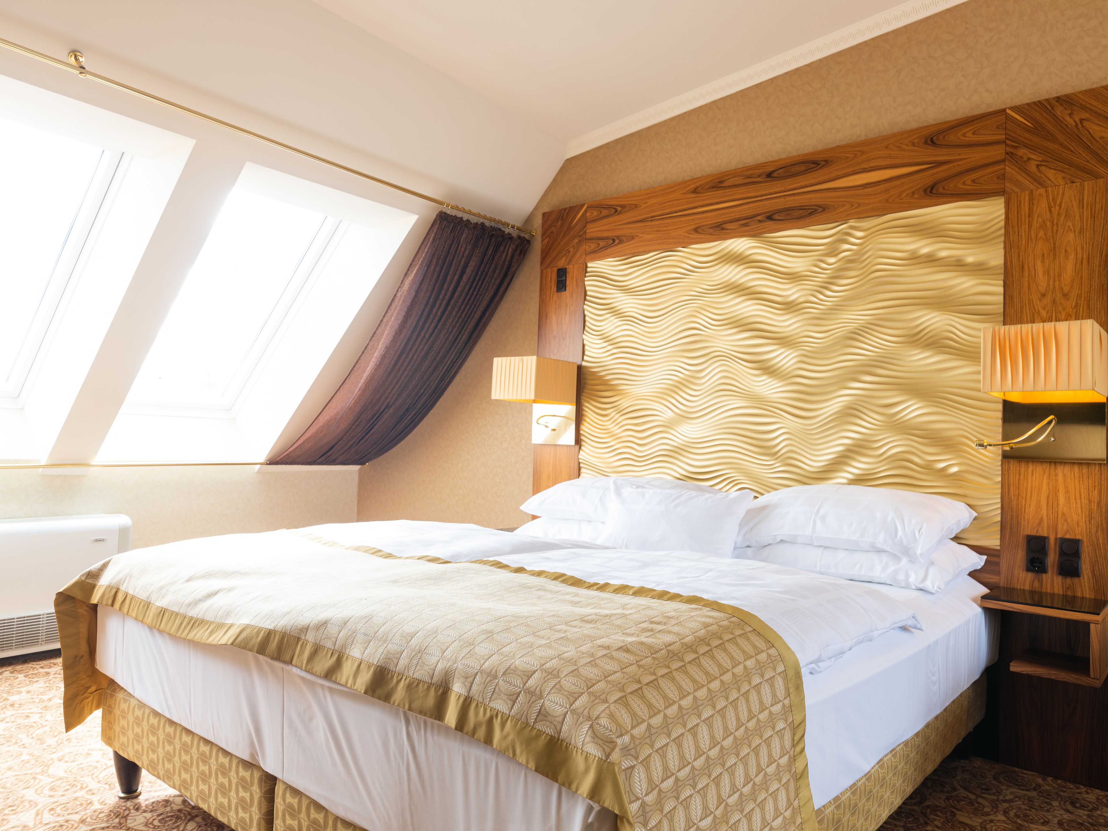 Quarto de hotel com cama grande, cabeceira de madeira, janela com cortinas e abajur.