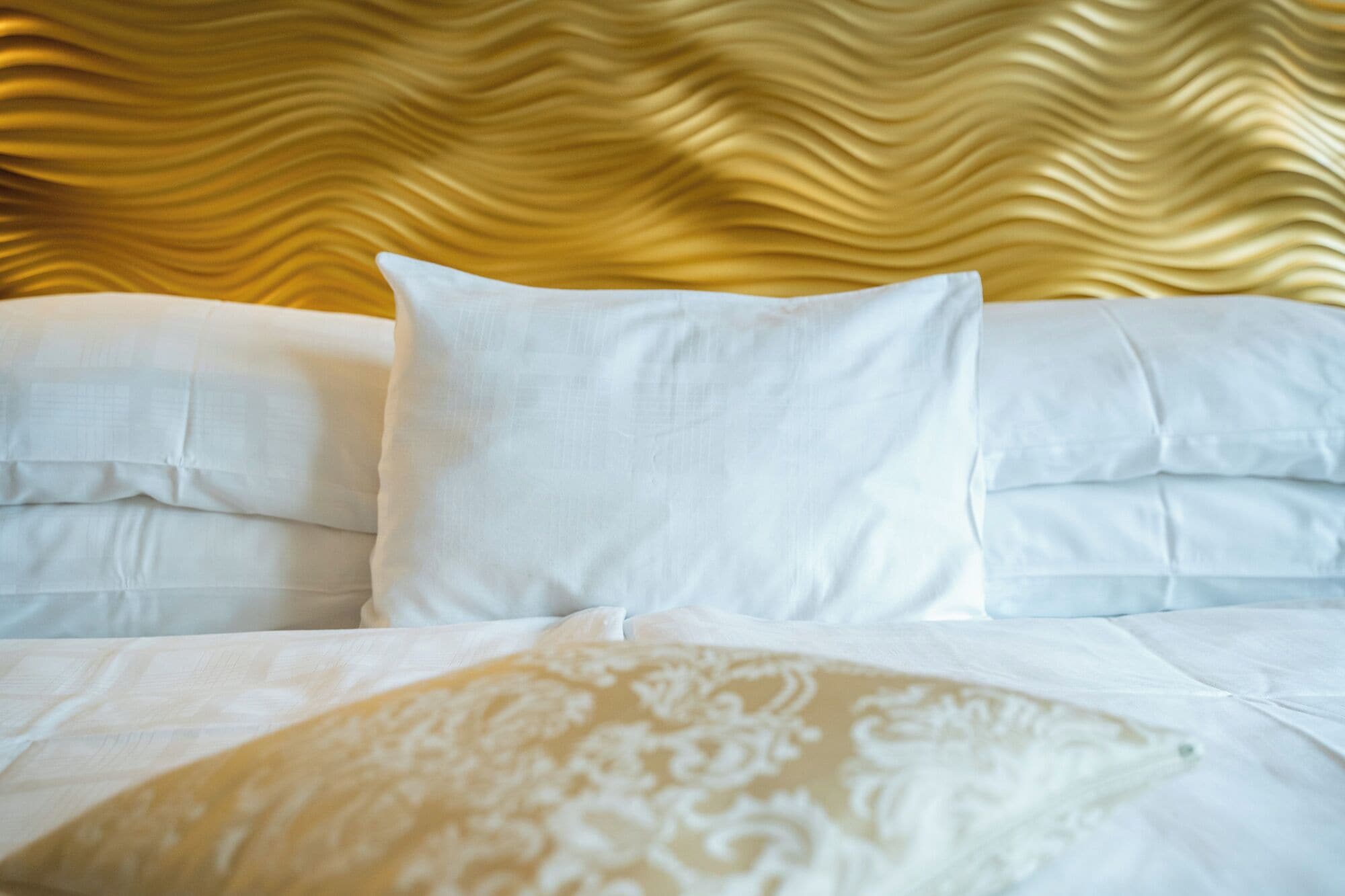 A neatly made bed with white linens and a patterned throw pillow.