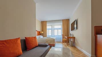 A hotel room with a bed, a sofa, a desk, and a TV.