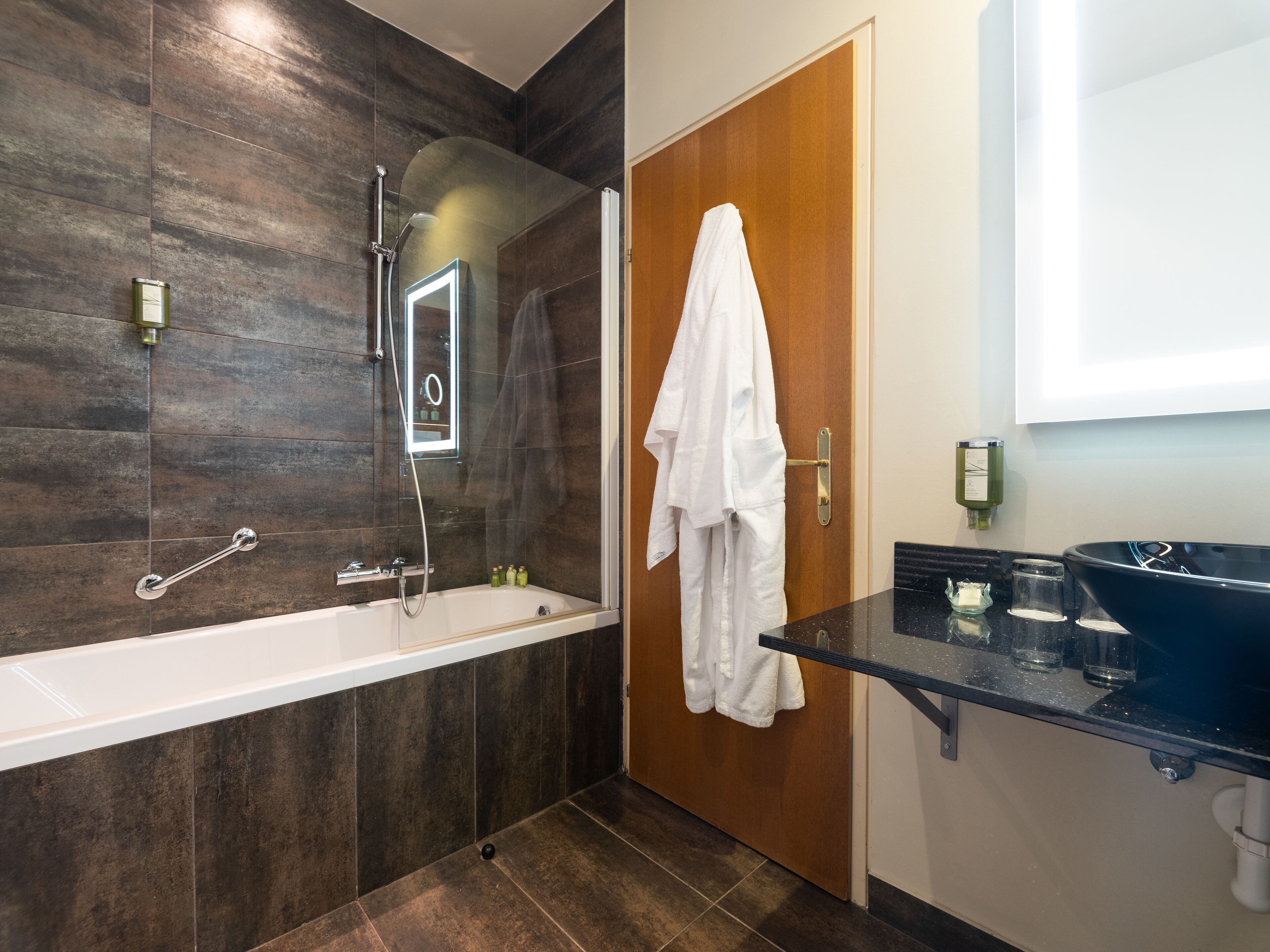 Un baño moderno con bañera, ducha con cerramiento de vidrio, puerta de madera y lavabo negro con recipiente de cristal.