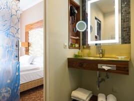 Casa de banho de hotel com toucador de madeira, espelho, lavatório e suporte para toalhas.