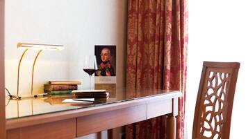 Uma mesa com uma luminária, livros, uma taça de vinho e um retrato emoldurado.