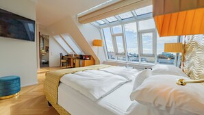 Un dormitorio con cama, escritorio, silla y ventana con vista a edificios.
