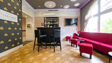 Un hall de hotel con zona de bar, un sofá rojo y un suelo estampado.