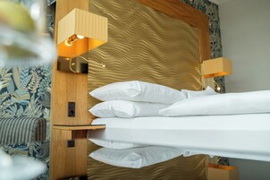 Cama bem arrumada com lençóis e almofadas brancos, cabeceira de madeira e duas luminárias fixadas na parede.