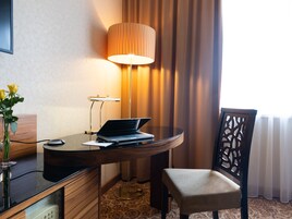 Ein Hotelzimmer mit Holztisch, Laptop, Lampe, Stuhl und einer Blumenvase.