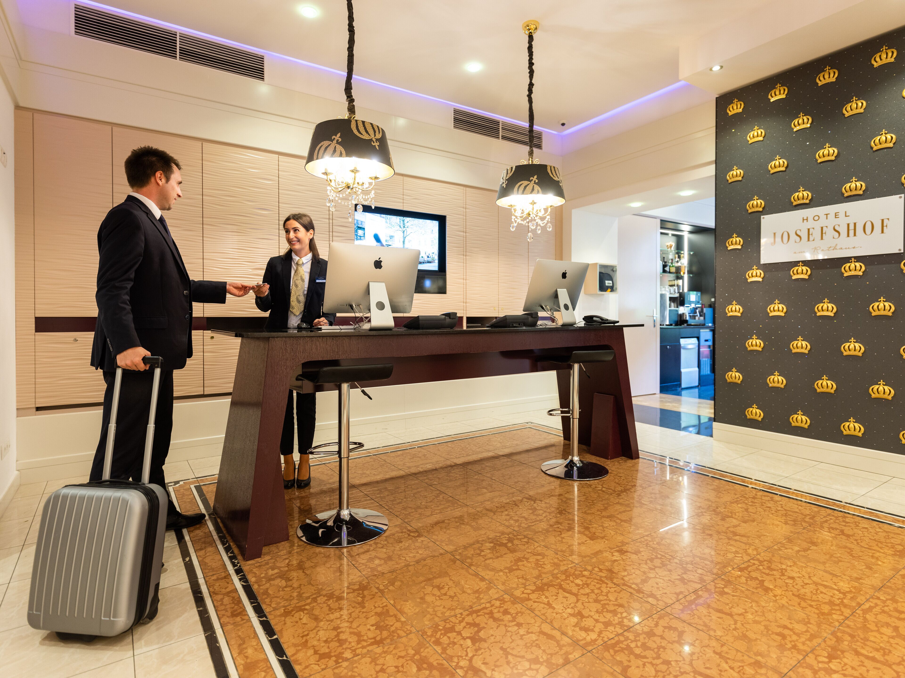 A hotel reception desk with a modern design, featuring a large screen, a computer, and a bar area.
