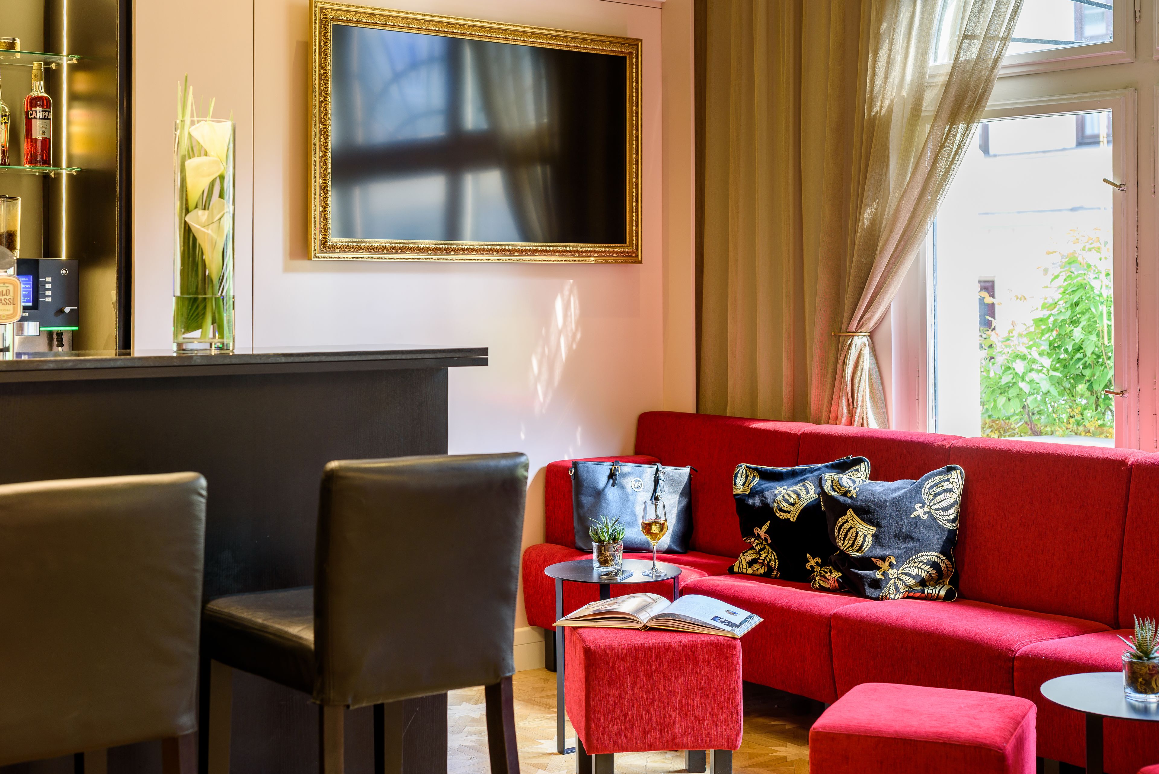 A modern living room with a red sofa, a small round table with a book and a glass, and a bar area with bottles and a TV.