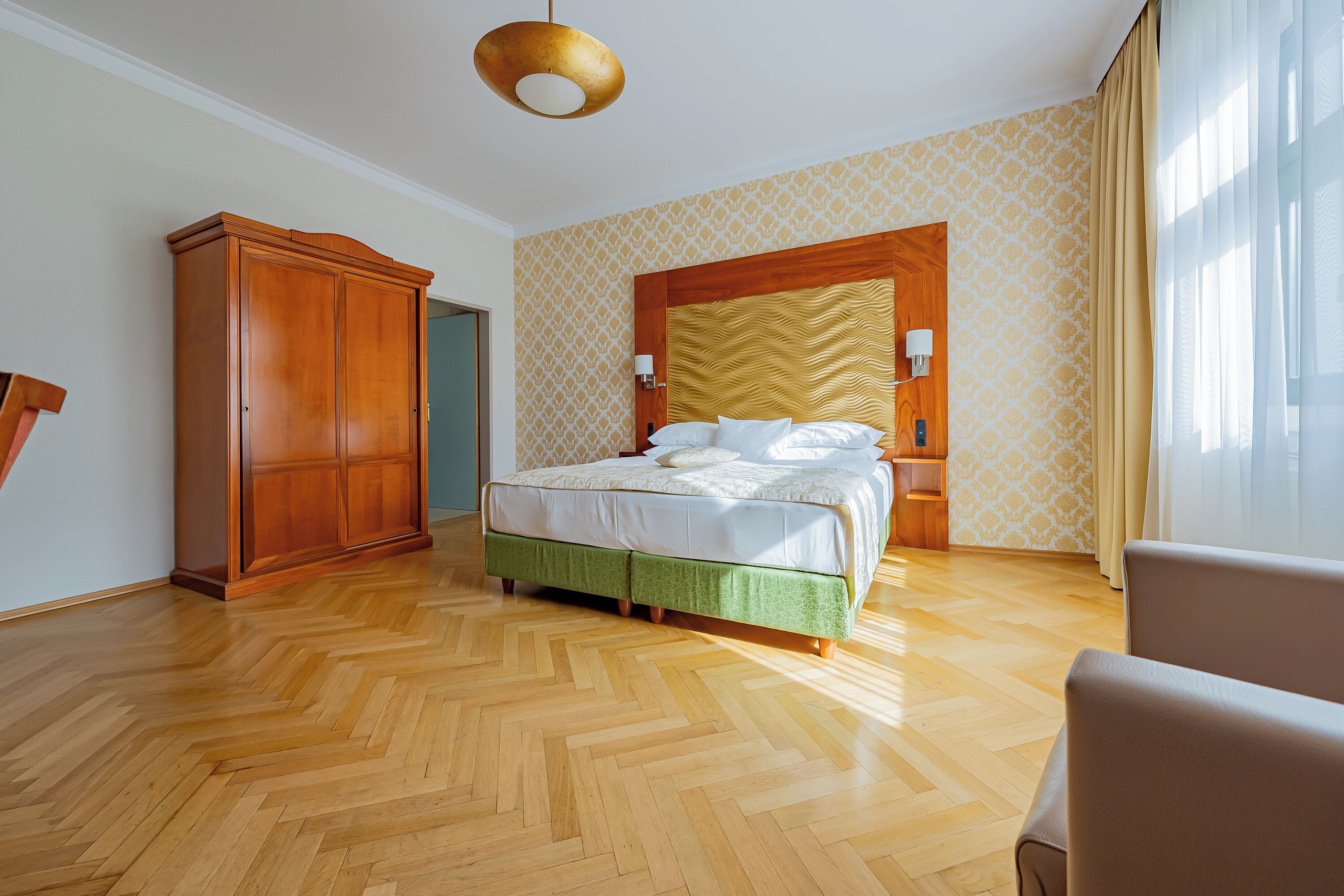 Ein Hotelzimmer mit Holzboden, einem Bett mit grüner Bettdecke, einem Kleiderschrank und einem großen Fenster mit Vorhängen.