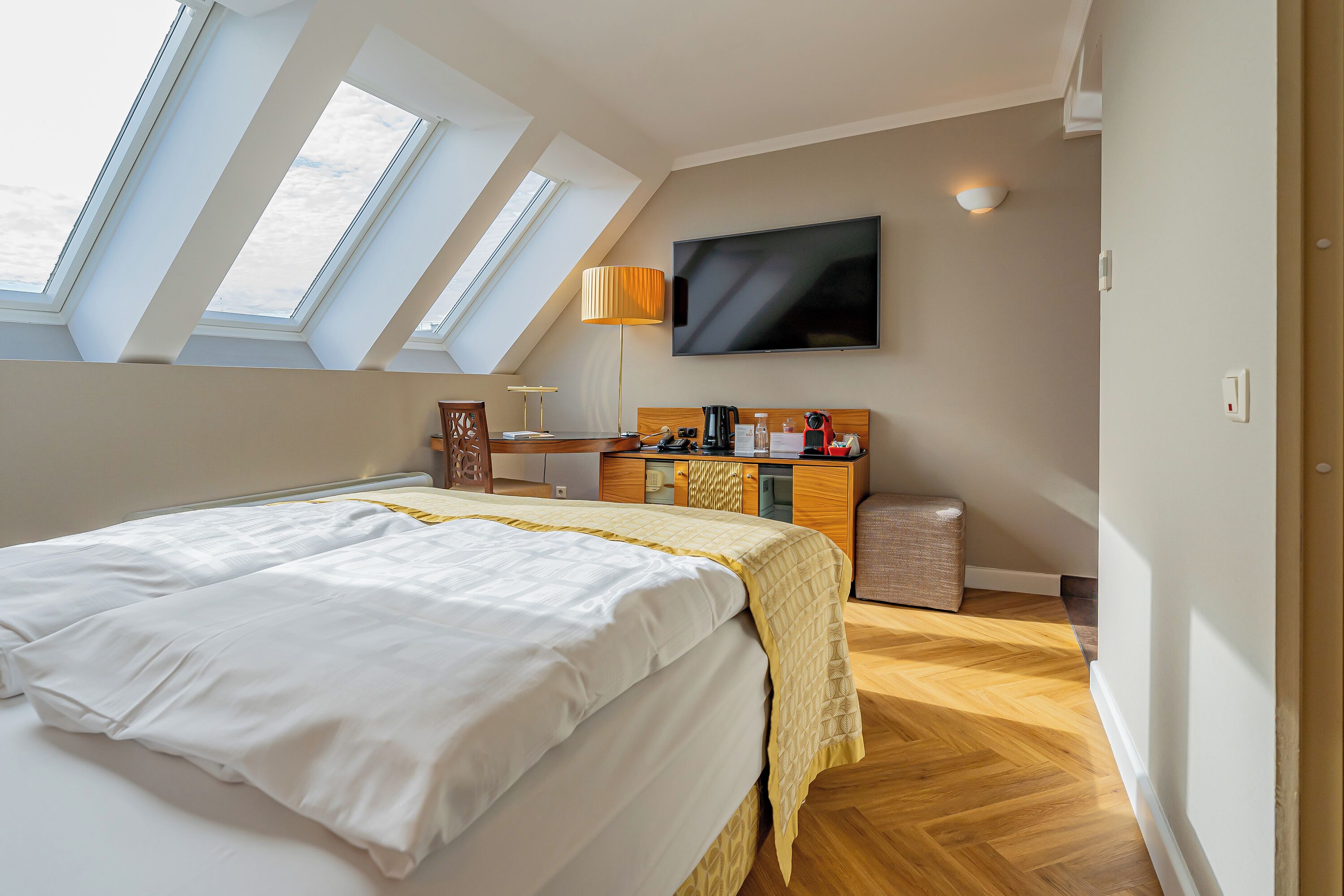 Une chambre d’hôtel moderne dotée d’un grand lit, d’un bureau, d’une télévision et de fenêtres de toit.