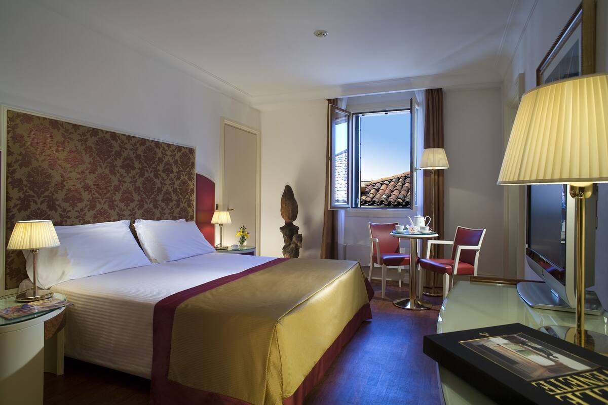 Ein Hotelzimmer mit einem großen Bett, einem Schreibtisch mit Stuhl, einem Fernseher und einem Fenster mit Blick.