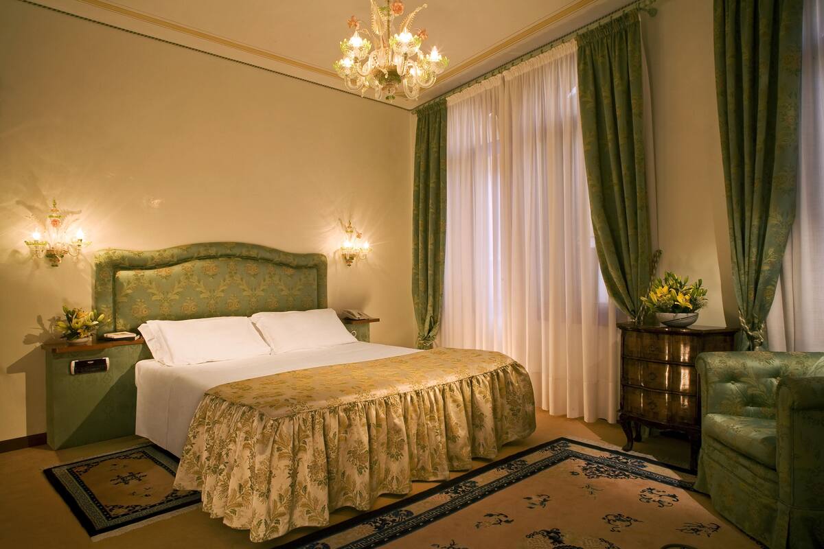 Ein Schlafzimmer mit einem großen Bett, grünen Vorhängen, einer Kristallleuchtre und einem grünen Sessel.