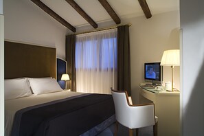 Quarto de hotel com uma cama, uma mesa com televisão, uma cadeira e uma luminária.