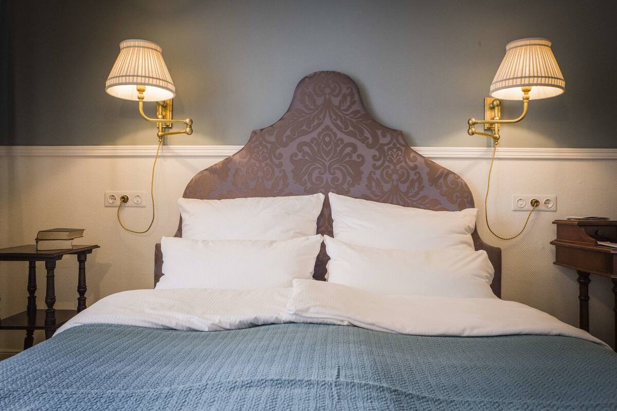 A neatly made bed with white linens, two bedside lamps, and a patterned headboard.