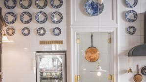 A kitchen with white tiled walls, a stainless steel refrigerator, a sink with a patterned backsplash, and a hanging light fixture. - Henri Hotel Berlin (Berlin)