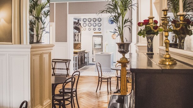A hallway with a wooden floor, a dining area with chairs, and a kitchen in the background. - Henri Hotel Berlin (Berlin)