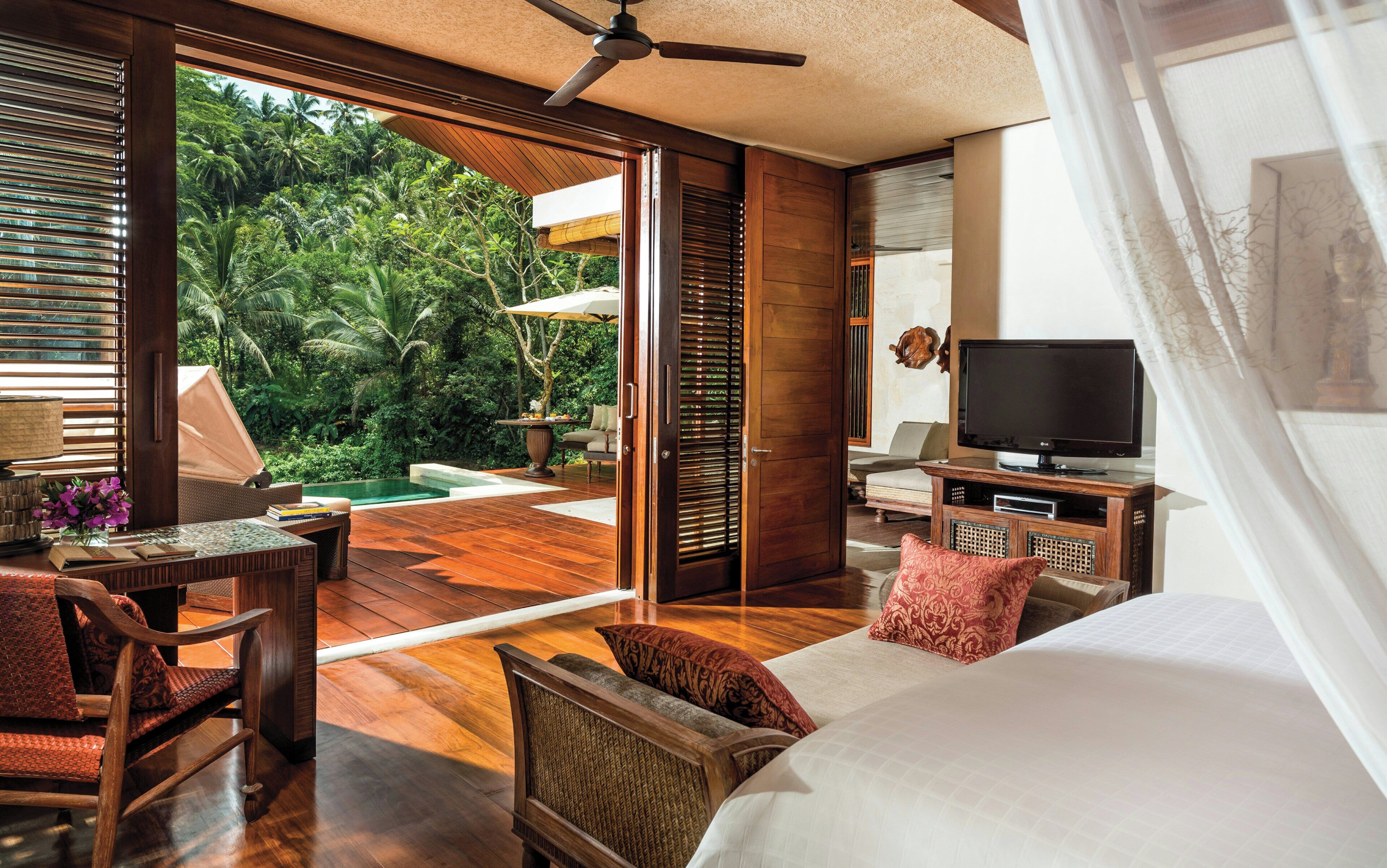 A modern room with a wooden floor, a bed, a TV, and a view of a lush garden.