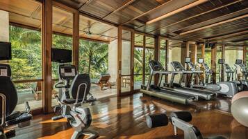 Un gimnasio con equipo de ejercicio, ventanas amplias y vistas a zonas verdes.