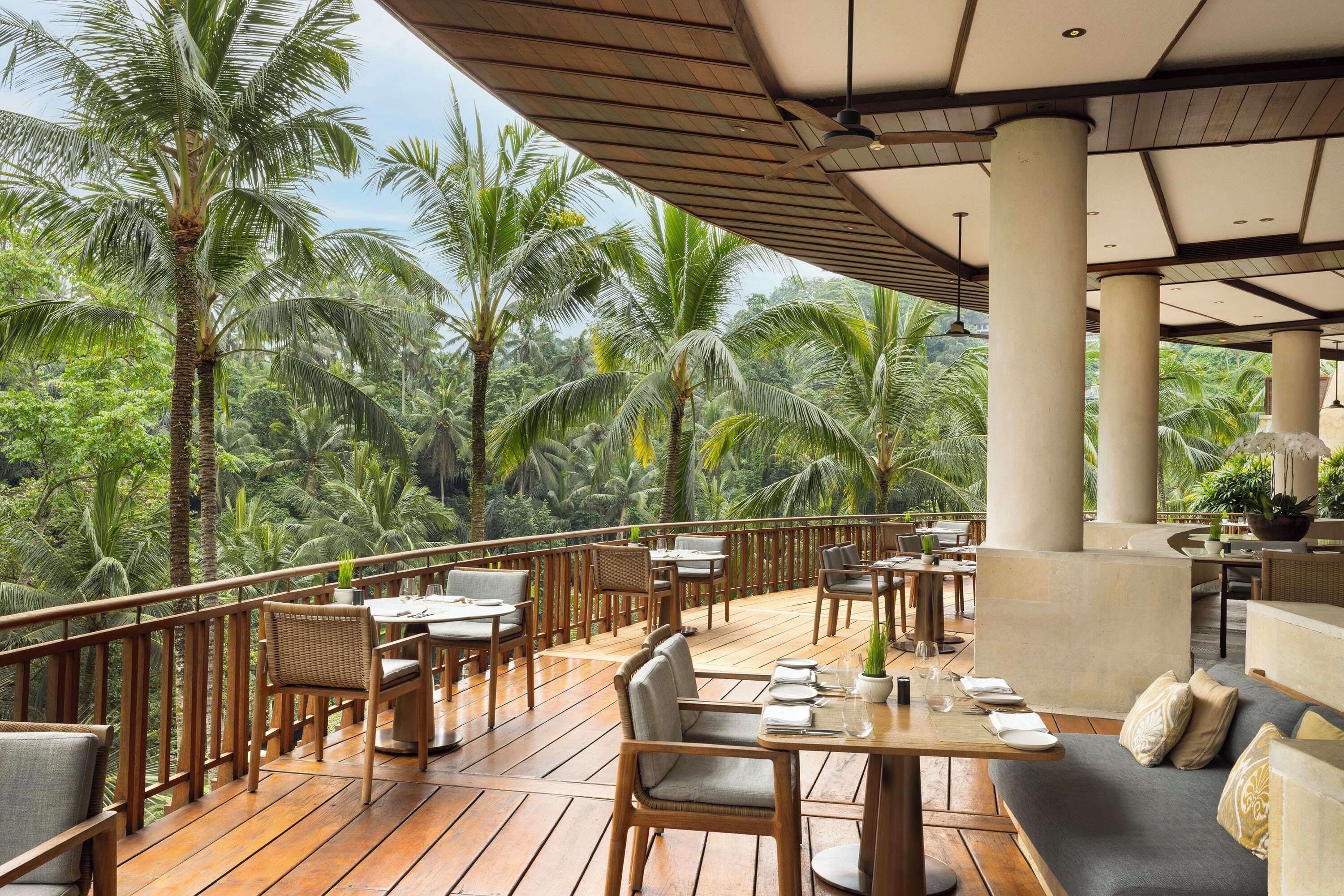 A wooden deck with tables and chairs, surrounded by palm trees.