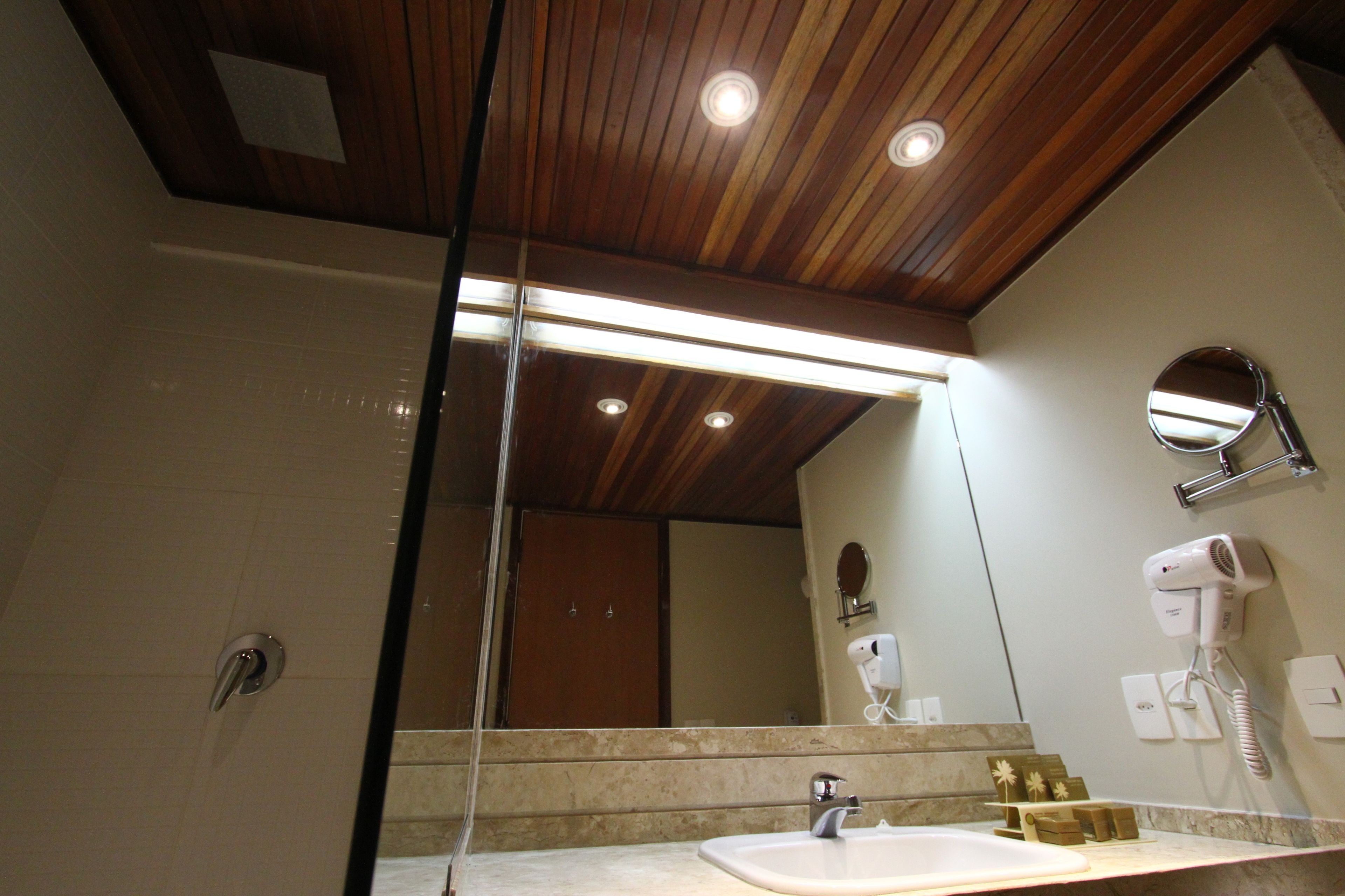 Un baño con techo de madera, un espejo, un lavamanos y un secador de pelo.