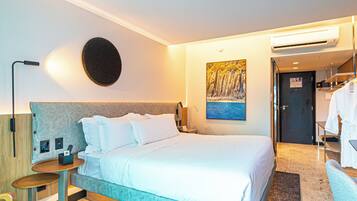 Habitación de hotel con cama, mesita de noche, lámpara, aire acondicionado y un cuadro en la pared.