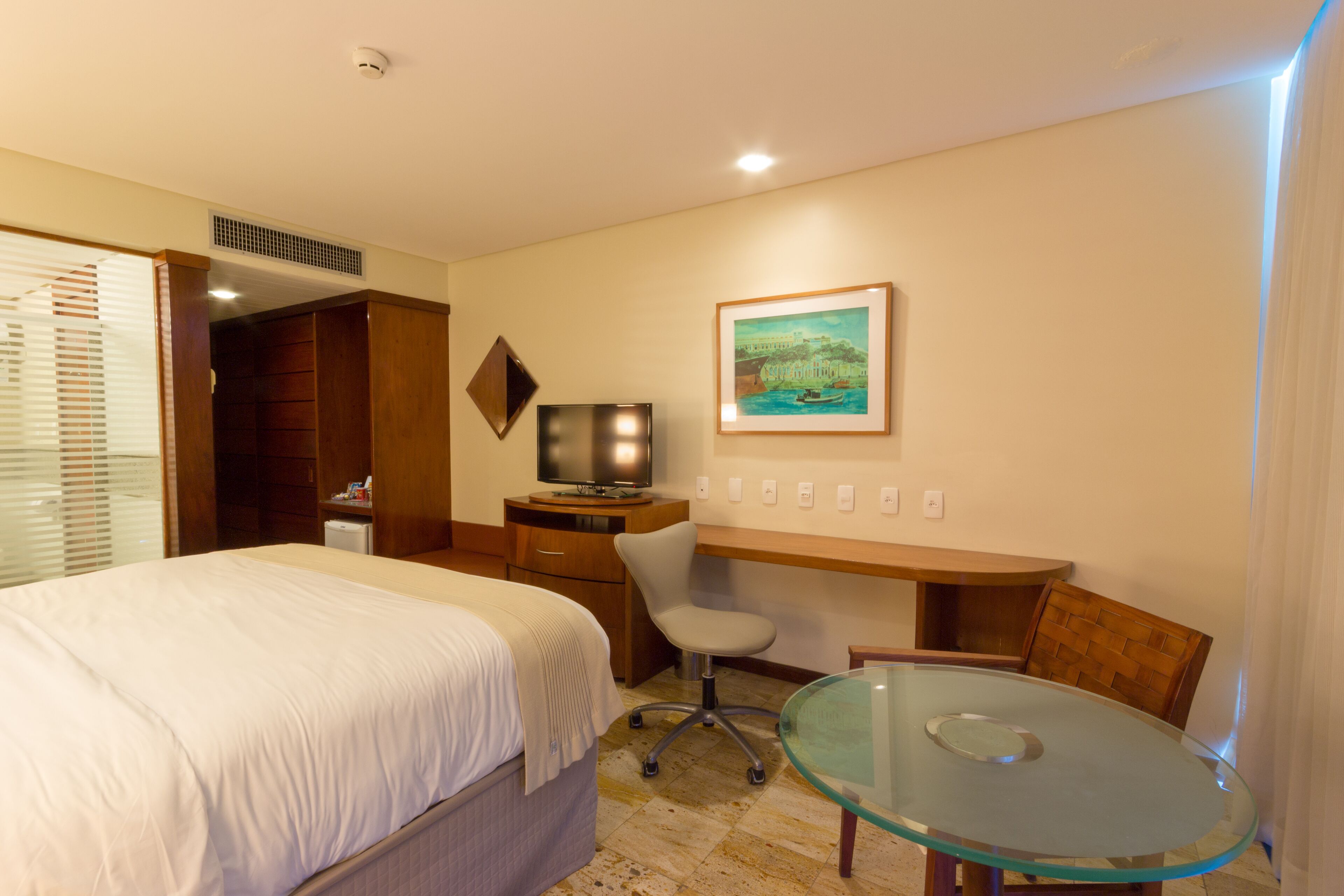 Una habitación de hotel con cama, escritorio, silla, televisor y un cuadro en la pared.