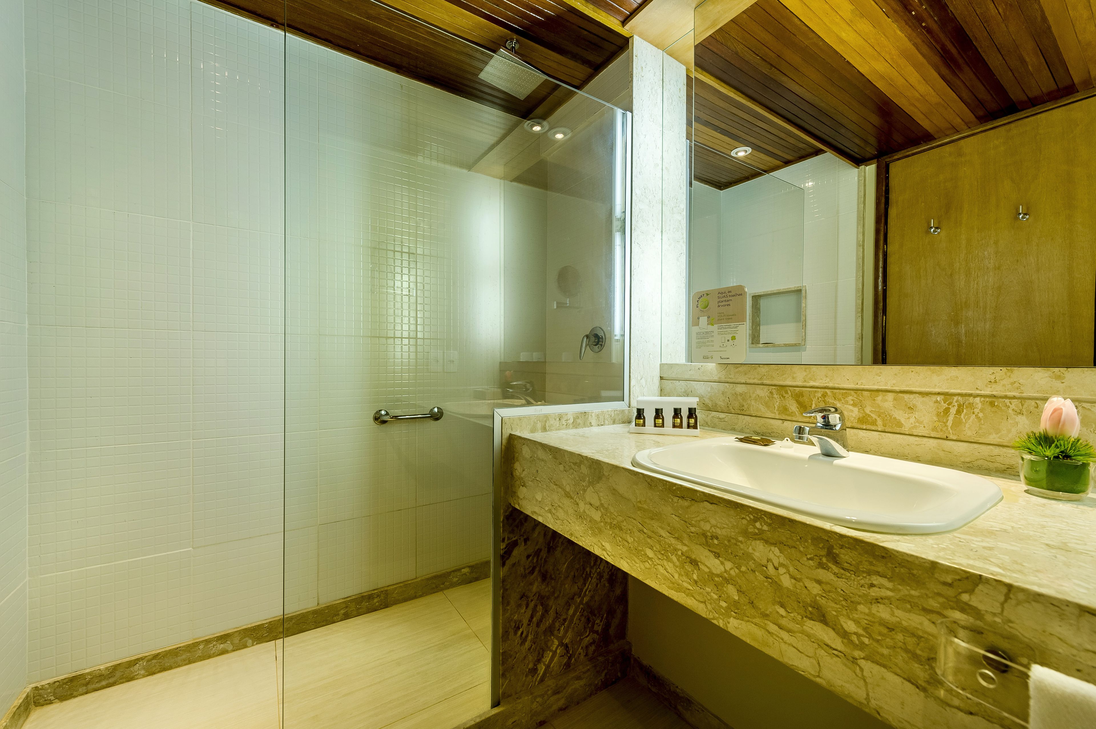A modern bathroom with a glass shower enclosure, a marble sink, and a wooden ceiling.
