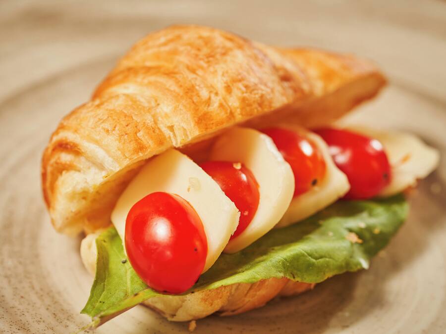 Un sándwich con un pan rústico, queso, tomates y lechuga.