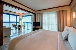 A hotel room with a large bed, a television, a desk with a chair, and a view of the sea through large windows. - Hotel Atlante Plaza (Recife)