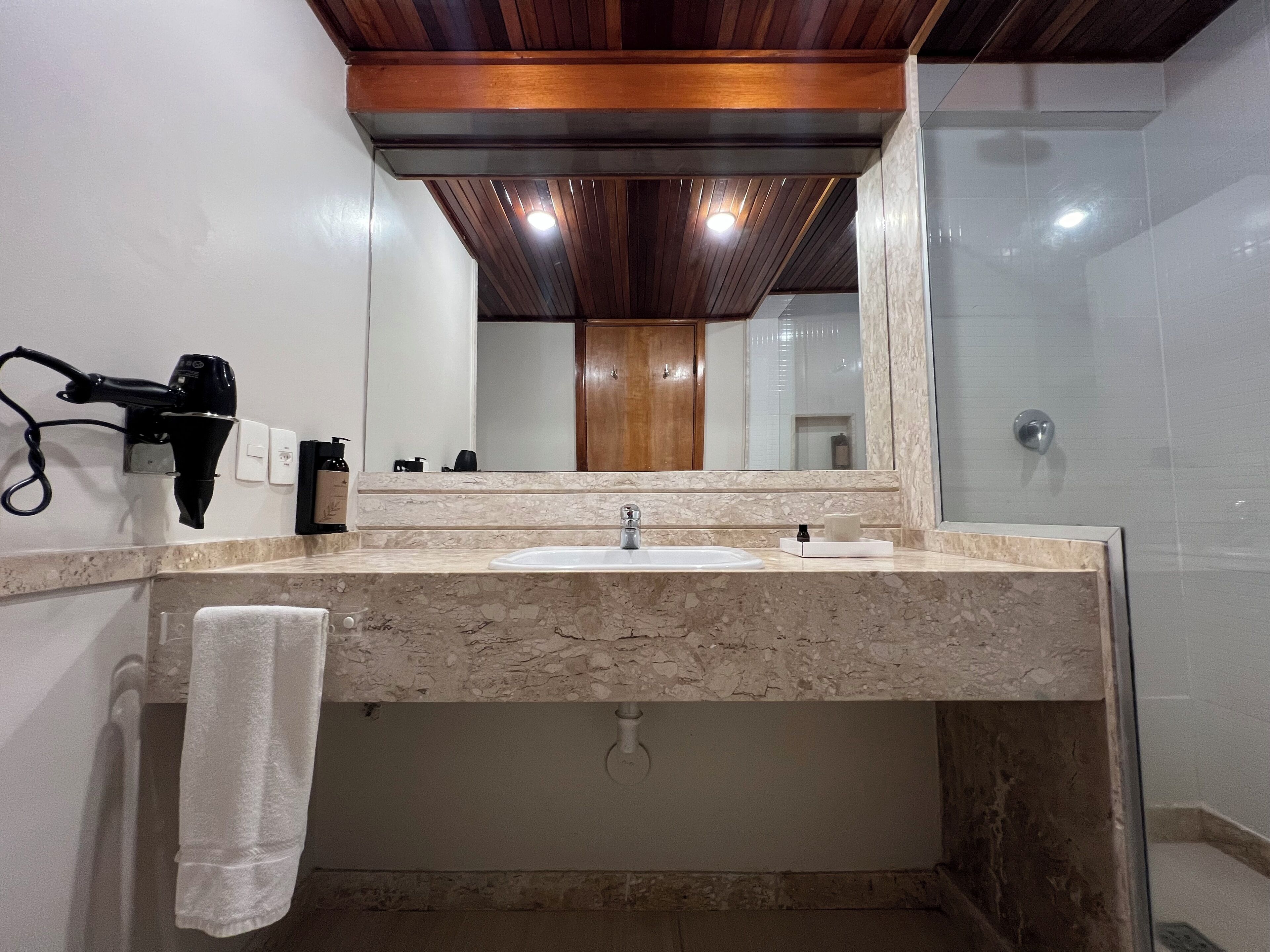 A bathroom with a marble sink, a towel hanging on the wall, a hairdryer, and a mirror.