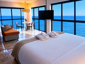 Habitación de hotel con una cama grande, un sofá, una mesa de comedor, sillas y vistas al océano.