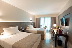 Habitación de hotel con dos camas, un escritorio, una silla, un televisor y una ventana con cortinas.