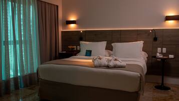Una habitación de hotel con una cama grande, dos mesitas de noche, una lámpara de pared y un ventanal con cortinas.