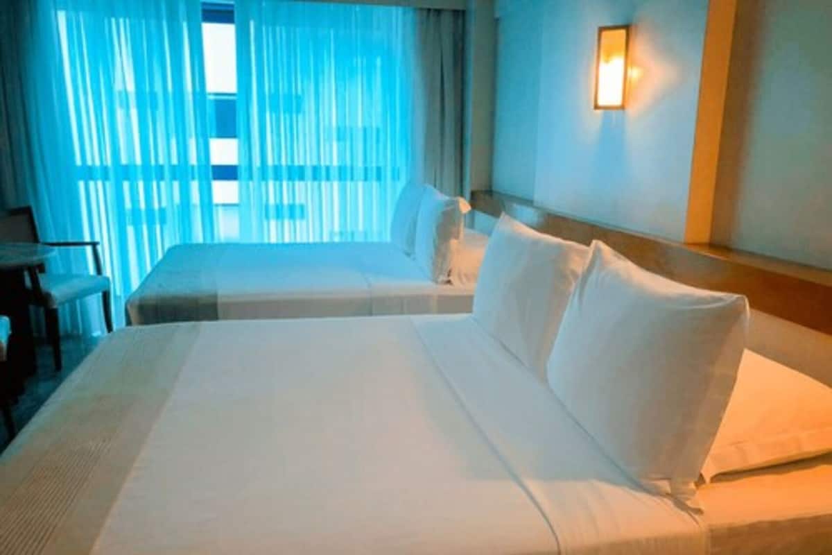 A hotel room with two beds, a desk, and a window with sheer curtains.