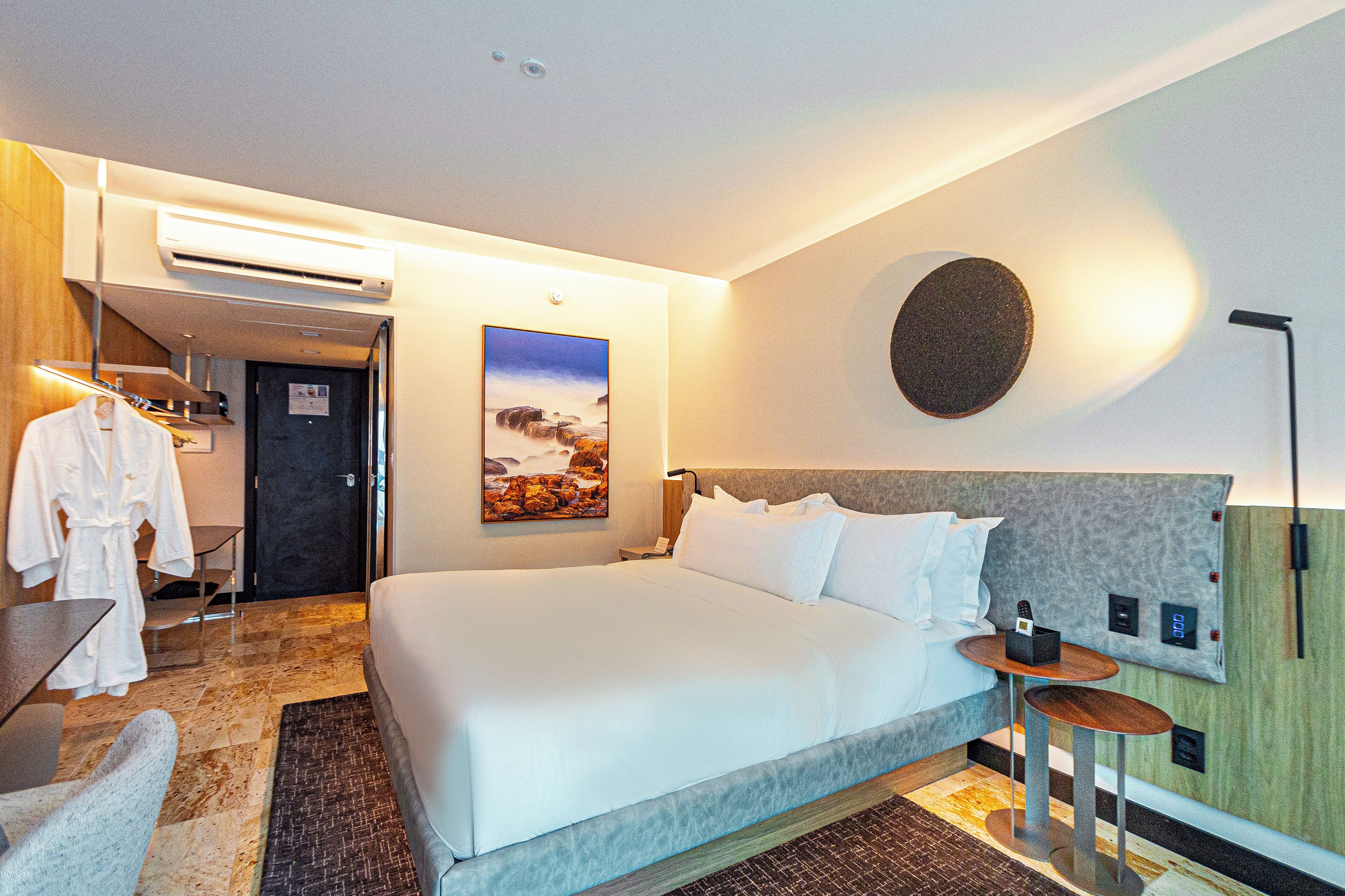 Une chambre d’hôtel avec un grand lit, un bureau, une chaise, un peignoir et un tableau au mur.