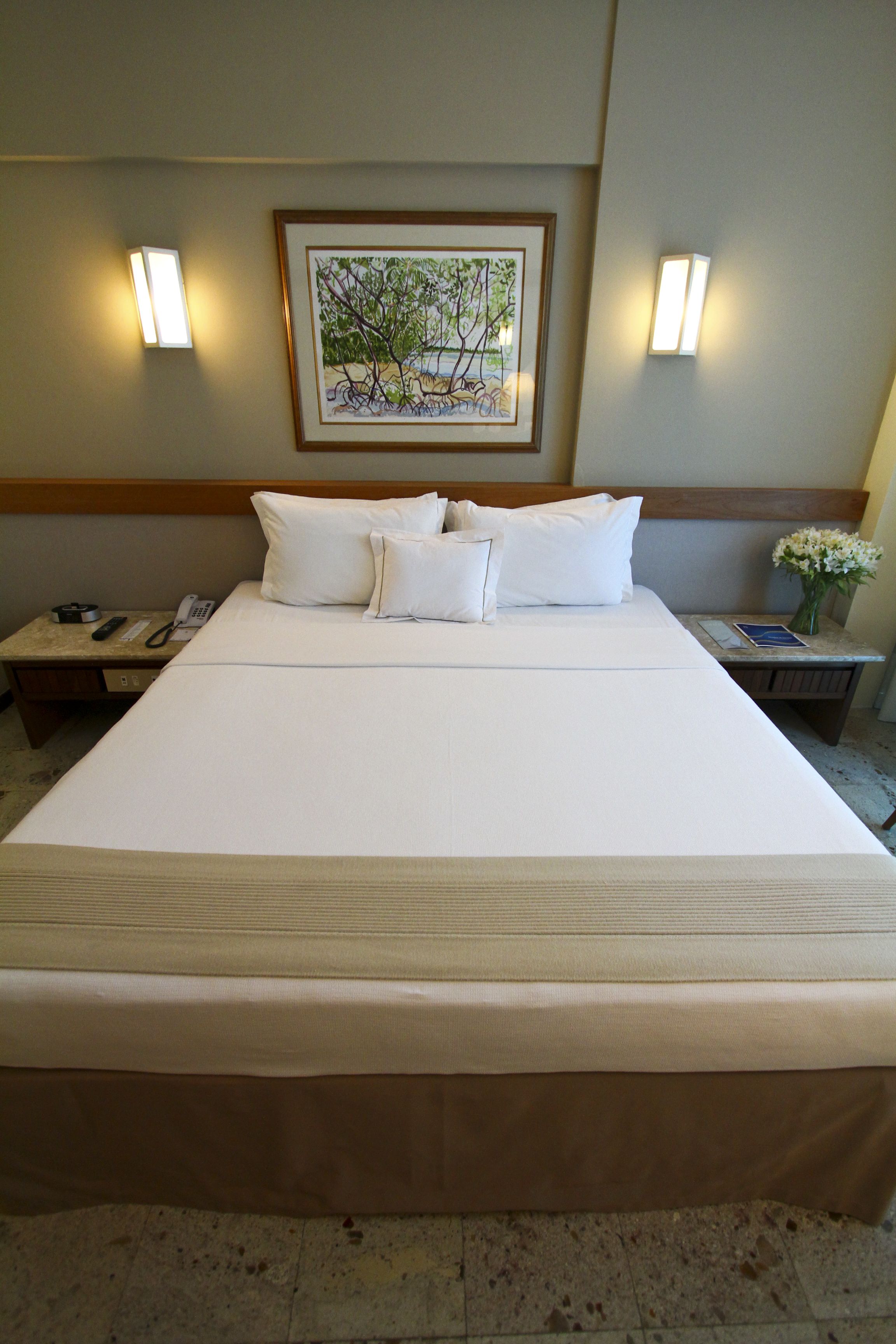 A hotel room with a large bed, two bedside tables, a framed artwork above the bed, and two wall-mounted lights.
