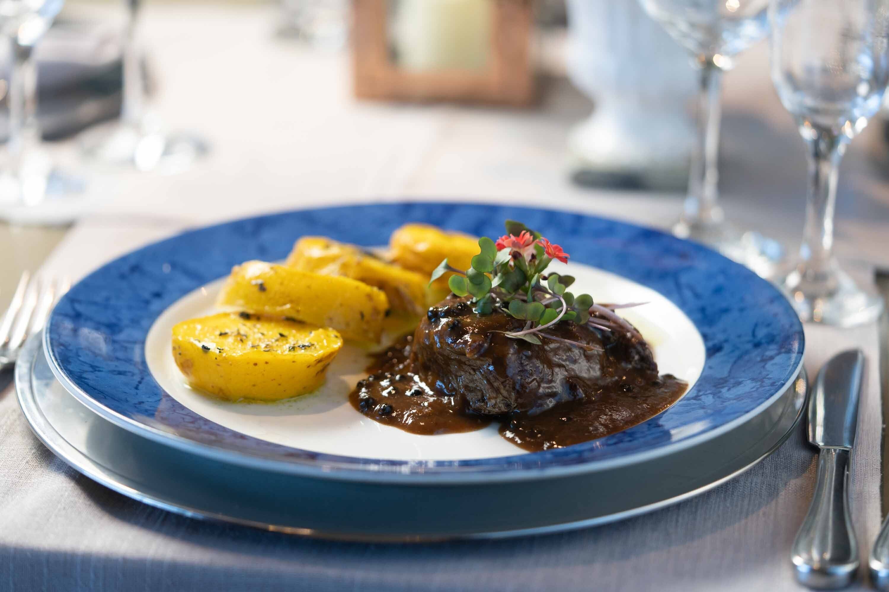 Ein Teller Essen mit blauem Rand, darunter ein Fleischgericht und Bratkartoffeln.