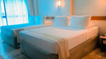 A hotel room with two beds, a large window with curtains, a wall-mounted light, and a bedside table.