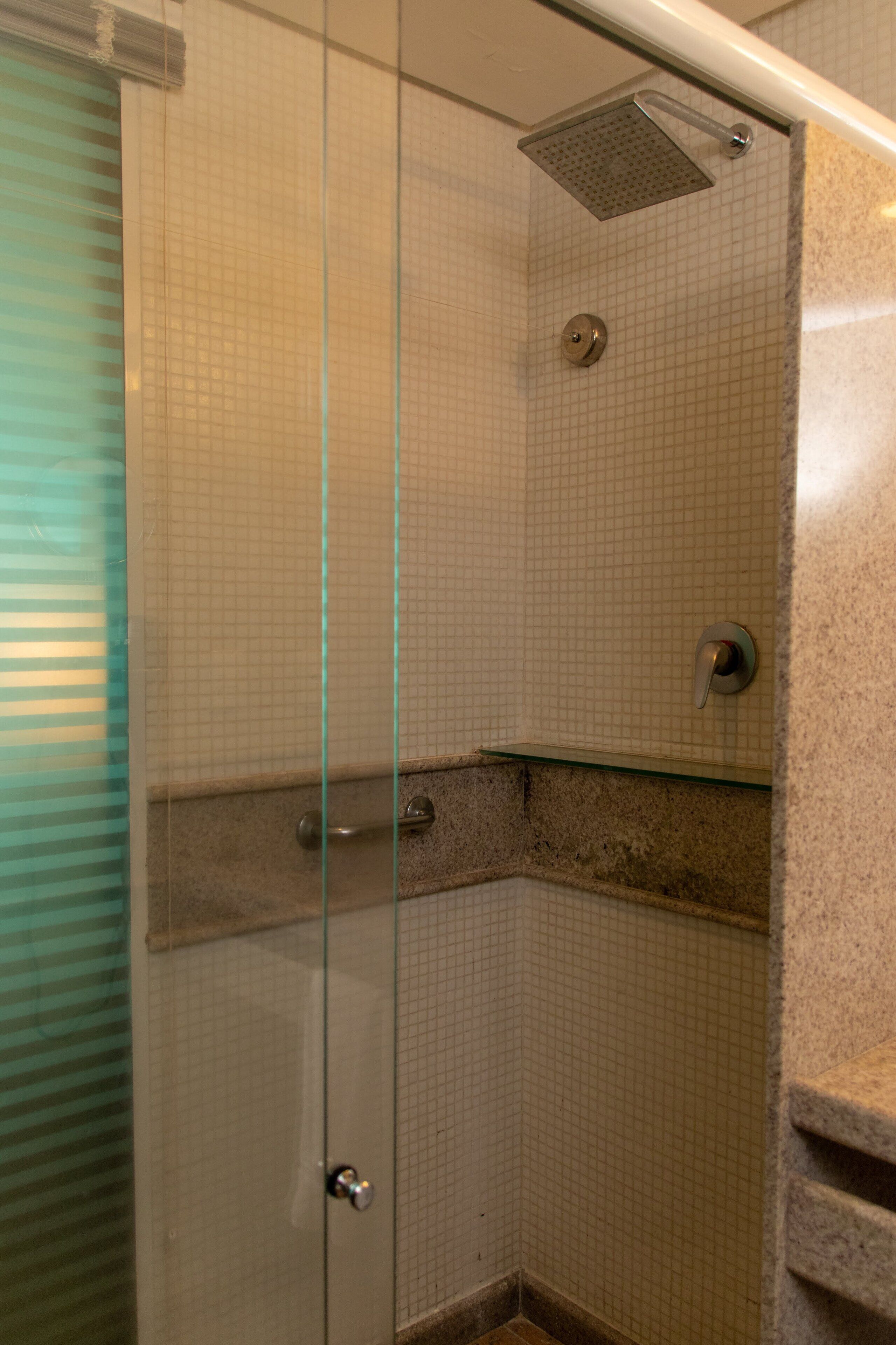 Une douche fermée par des parois de verre, avec un mur carrelé, une pomme de douche et un robinet de réglage.