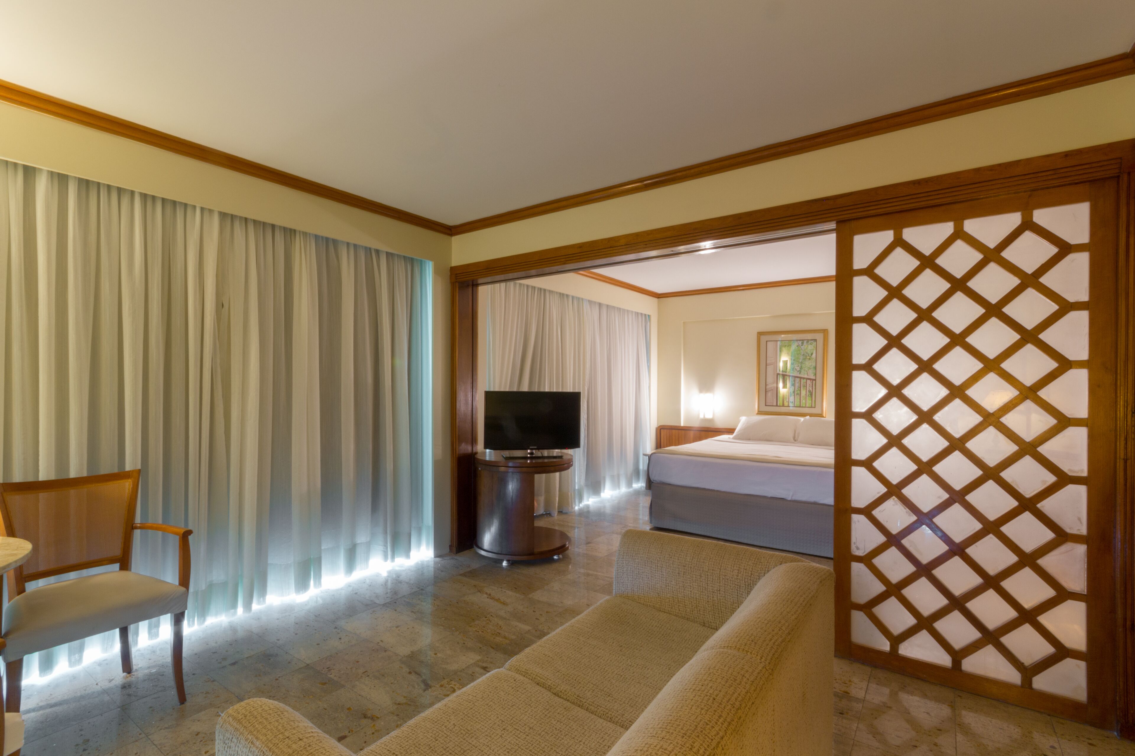 A hotel room with a bed, a TV, a sofa, and a chair.