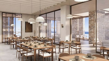 Un comedor amplio con varias mesas y sillas, ventanas grandes que ofrecen vista al mar, e iluminación colgante moderna.