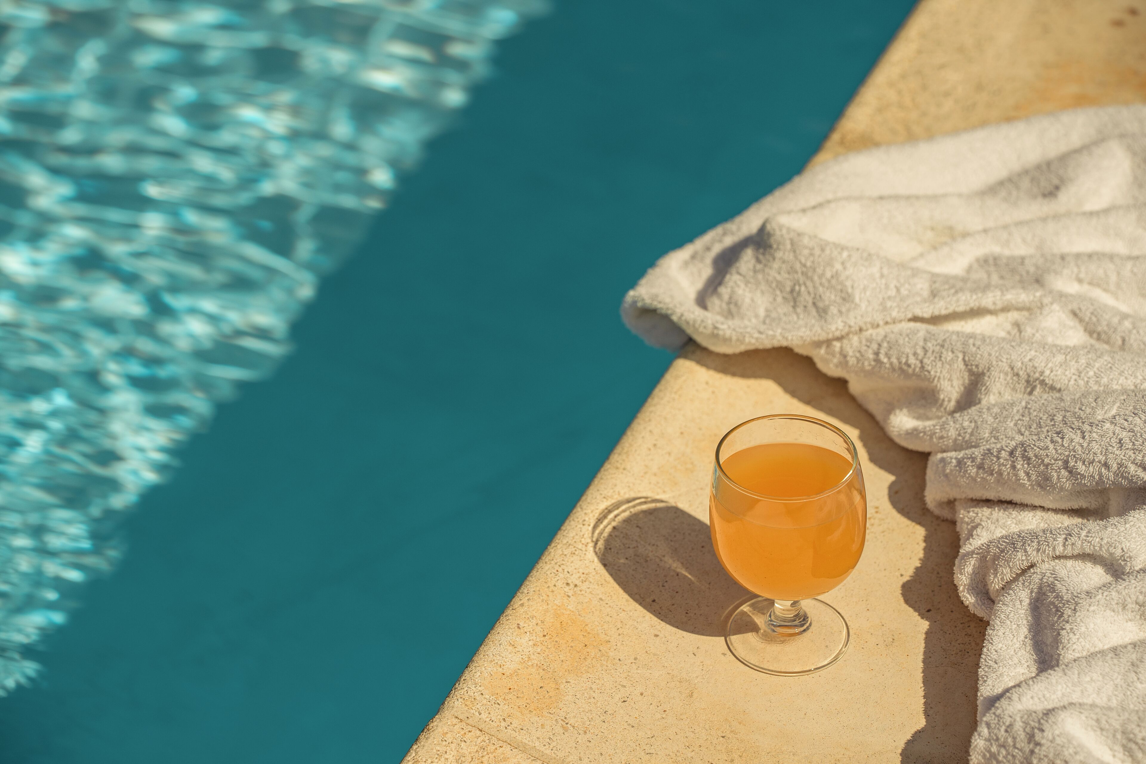 A glass of orange beverage on a poolside with a towel.