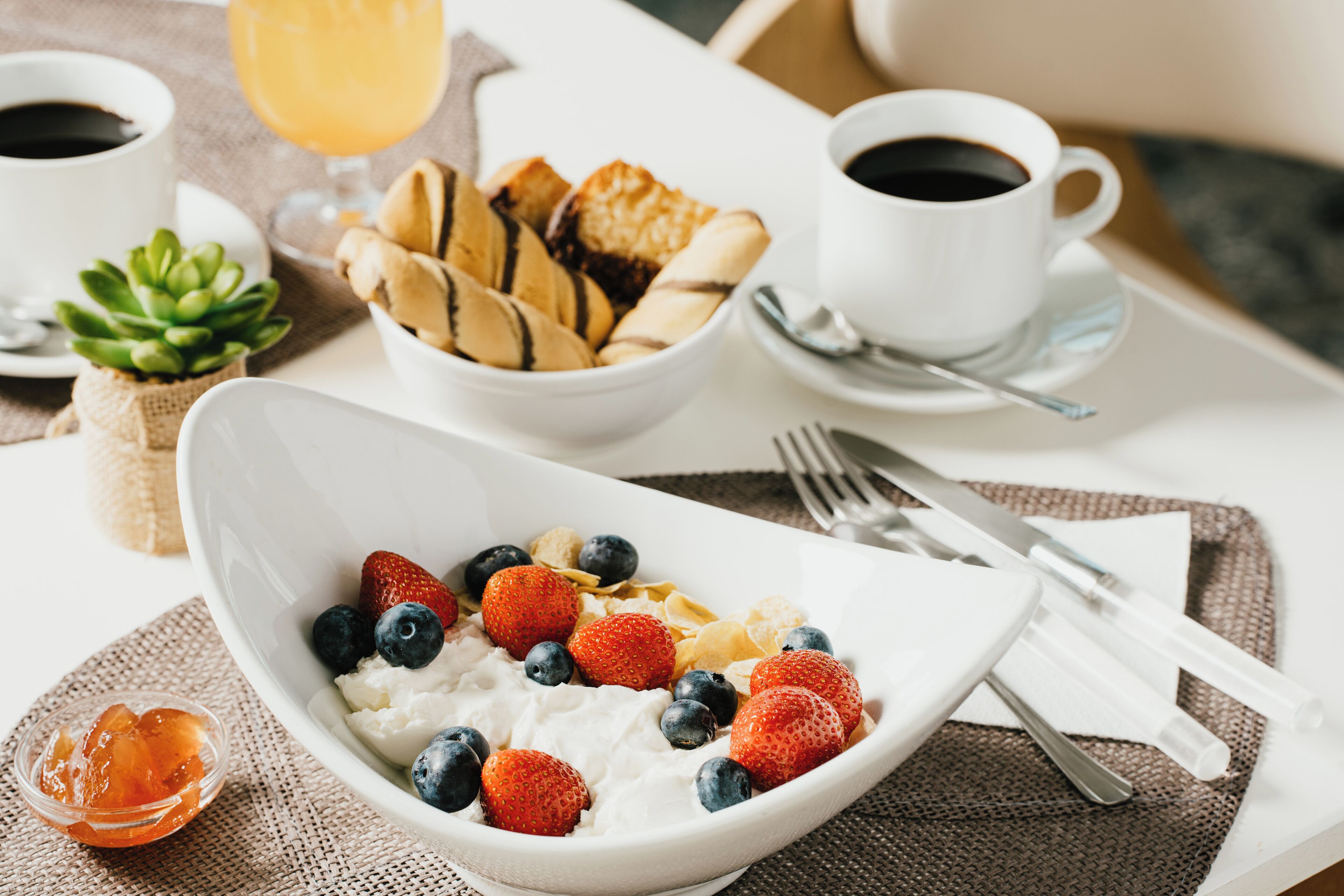 A breakfast setting with a bowl of yogurt topped with strawberries and blueberries, a glass of orange juice, and a cup of coffee.