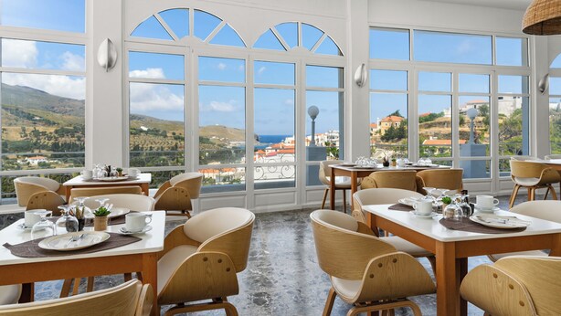 Comedor con mesas dispuestas para el desayuno, ventanas amplias con una vista panorámica y un suelo de concreto pulido.