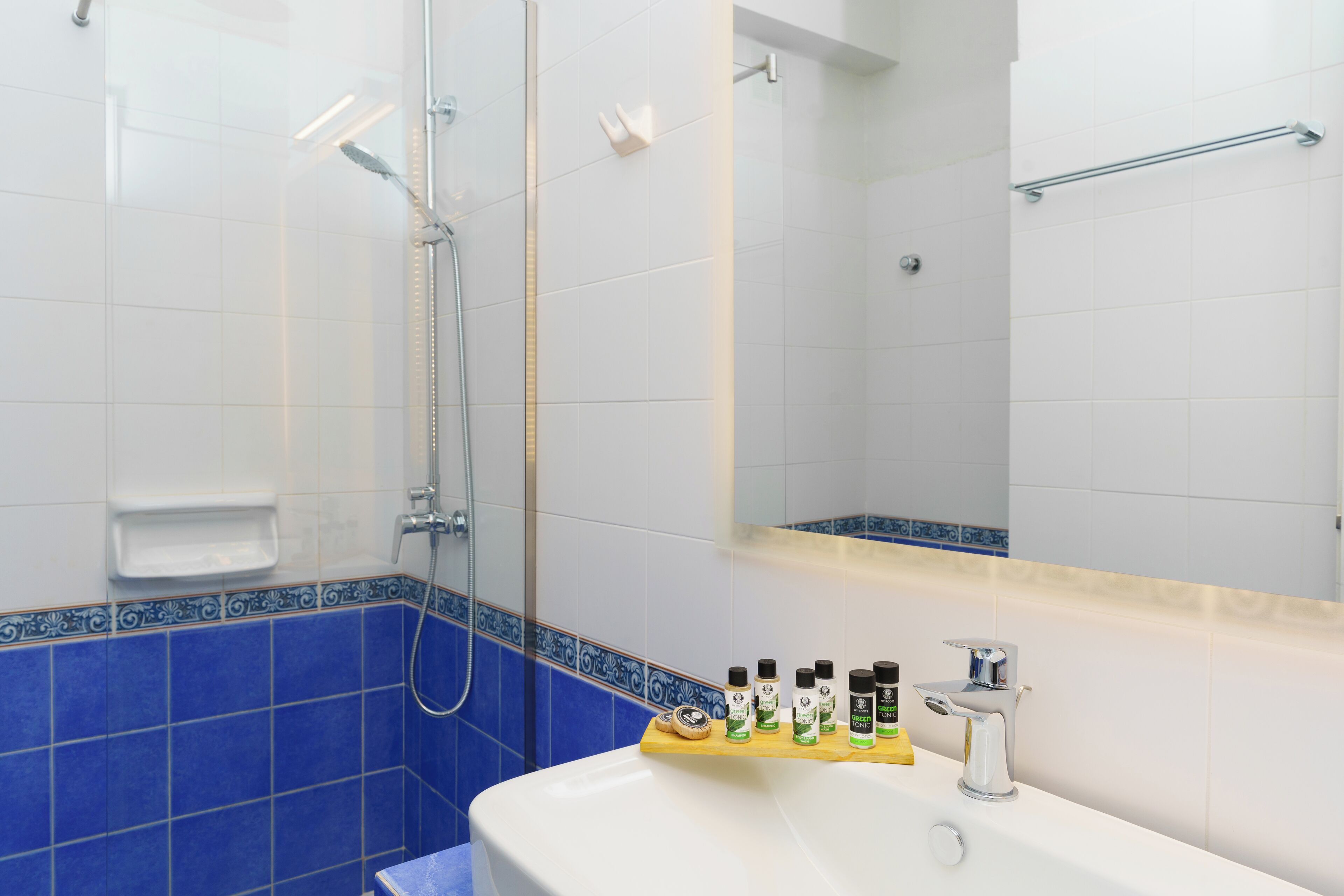 A bathroom with a white sink, blue-tiled walls, a handheld showerhead, and a mirror with a towel rack.