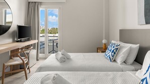 Habitación de hotel con cama, escritorio con televisor, silla y ventana con vista a edificios y árboles.