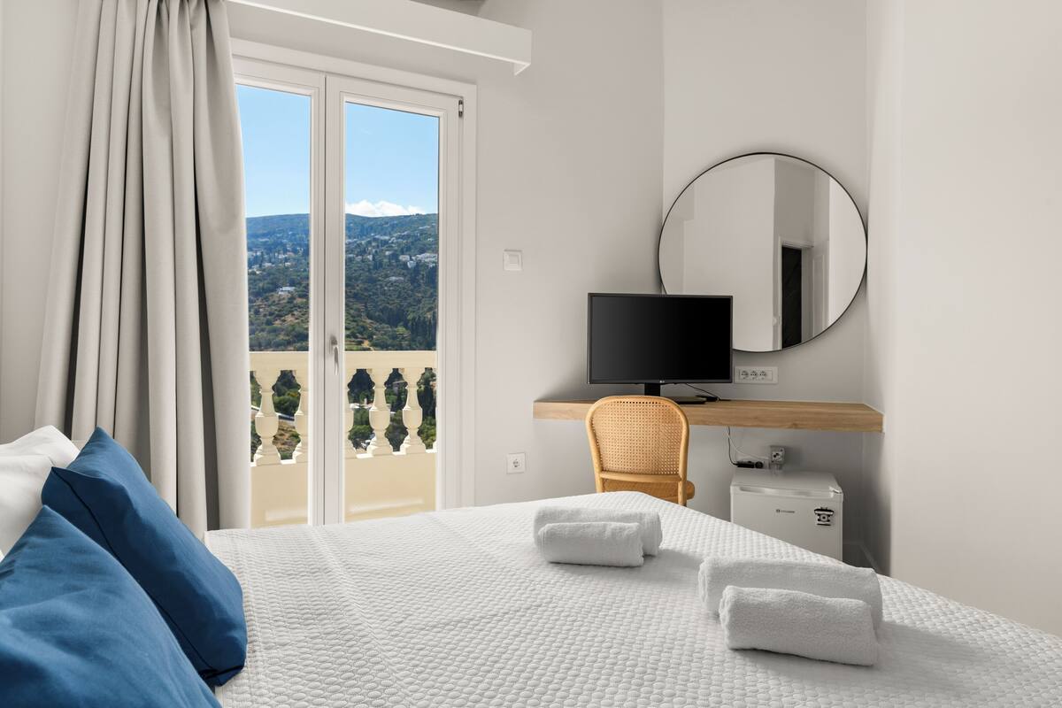 A hotel room with a bed, a TV, a chair, and a view of the outdoors.