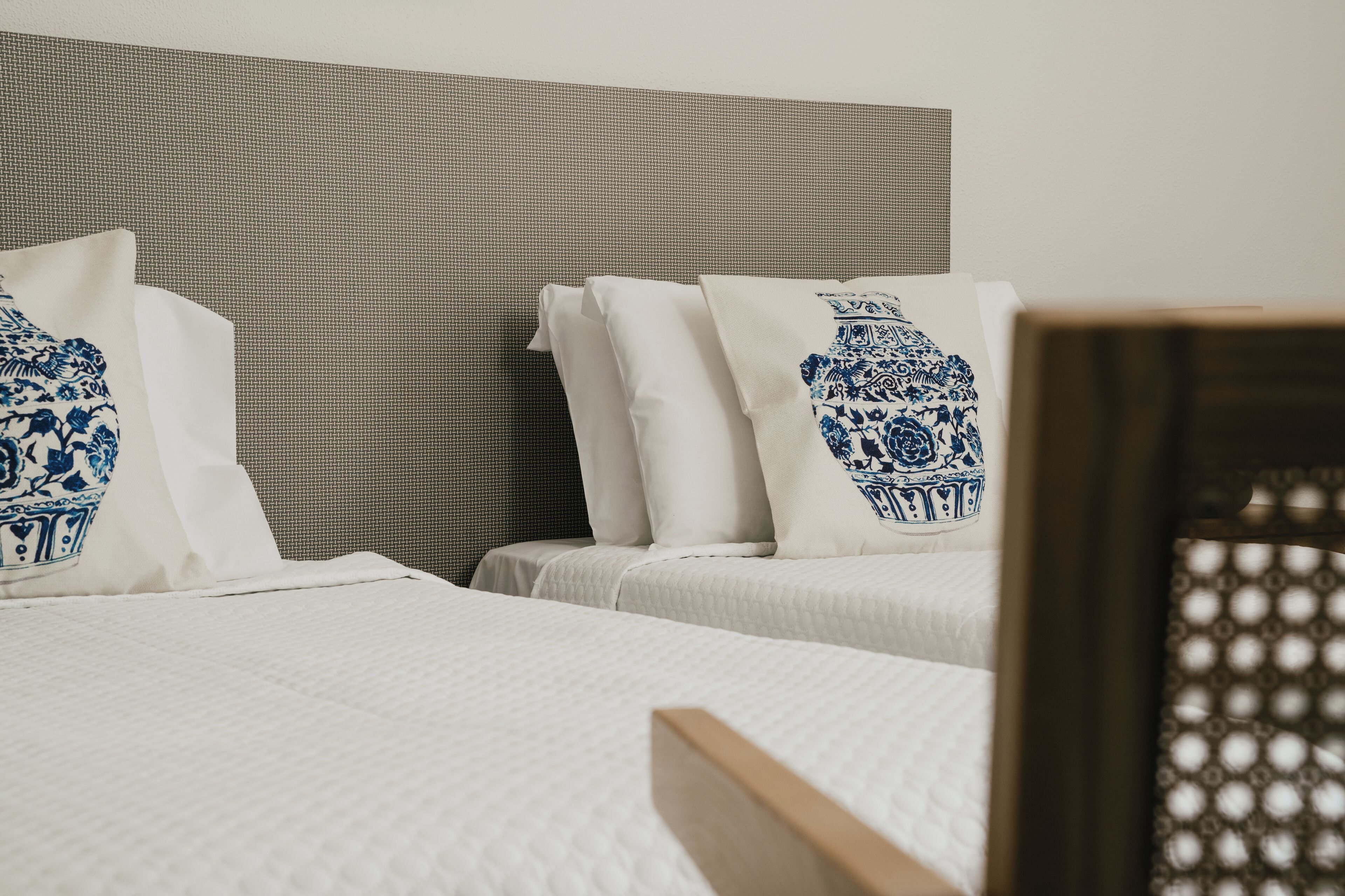 A hotel room with two beds, each with white bedding and blue floral pillows.