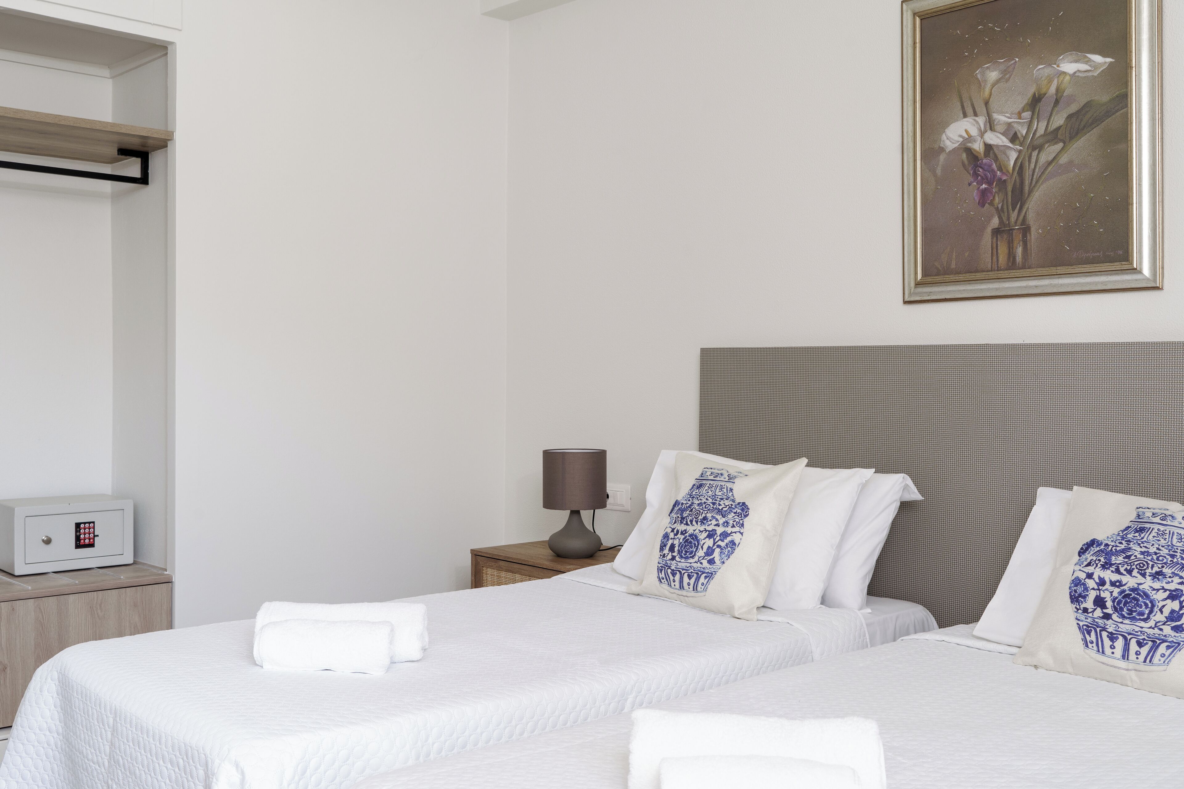 Una camera d'albergo con due letti, un comodino con una lampada, una cassaforte e un quadro appeso al muro.